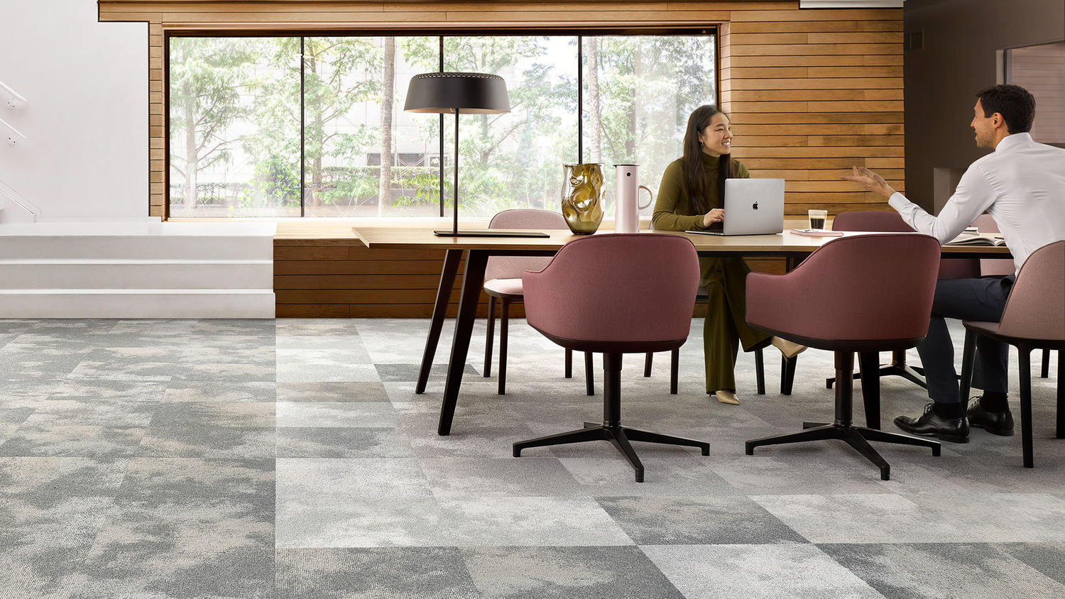 Een kantoor met tapijttegelvloeren met een vrouw en een man die aan een tafel werken en praten