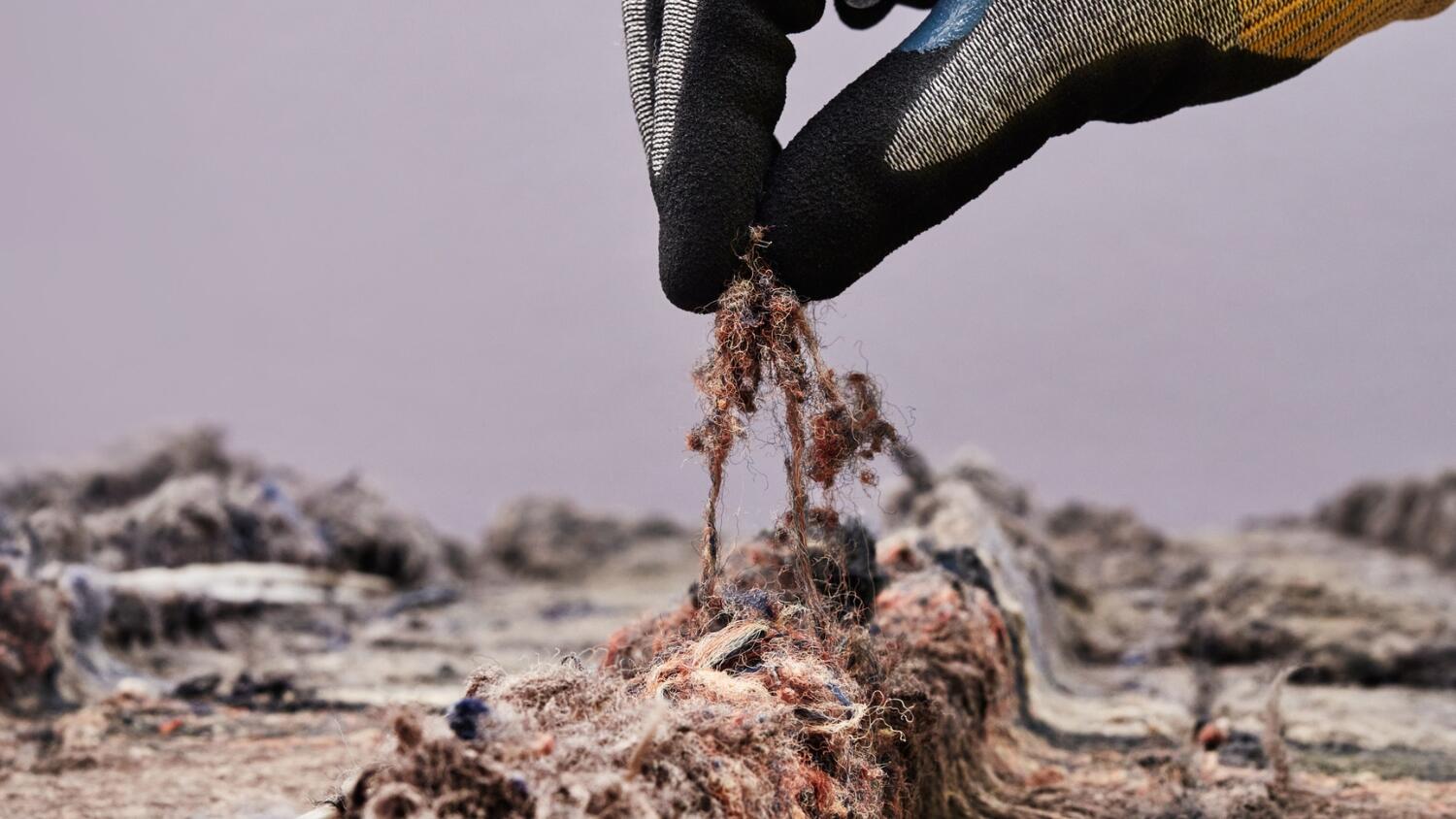 Close-up of a hand in a production glove holding a small bundle of recycled yarn from DESSO carpet tiles